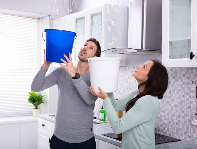 Couple Collecting Water Leaking From Ceiling In Bucket